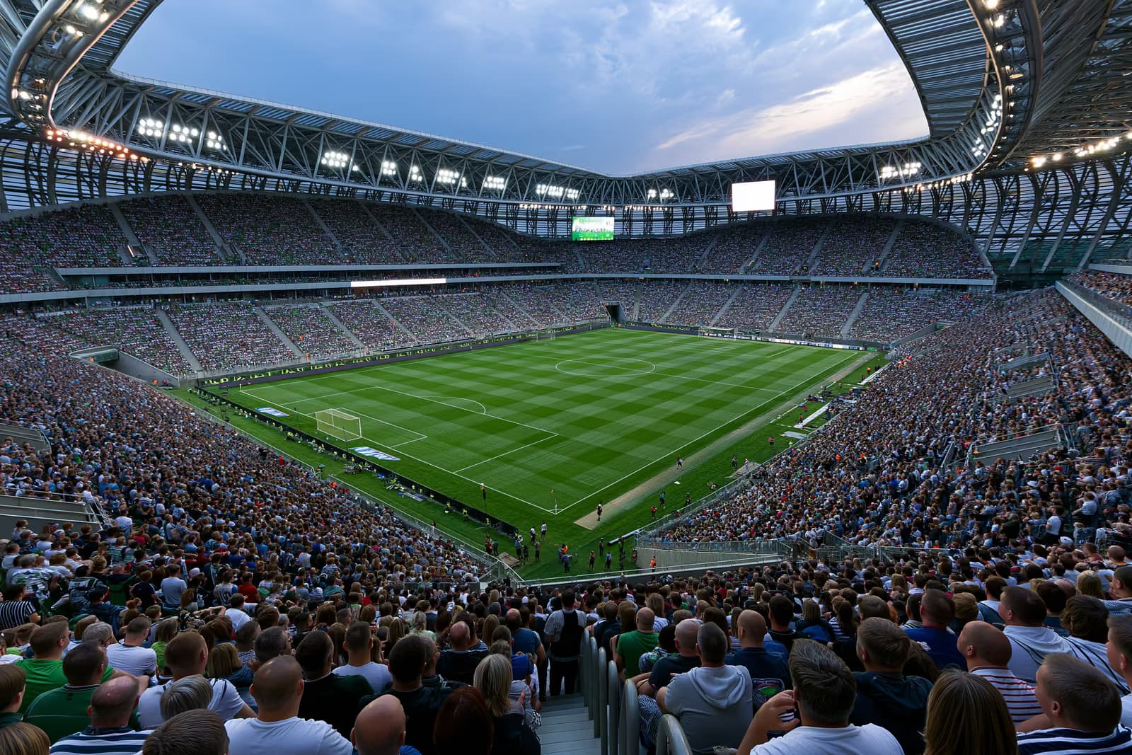 Un stadion mare de fotbal plin de fani sub reflectoare într-o seară de vară.