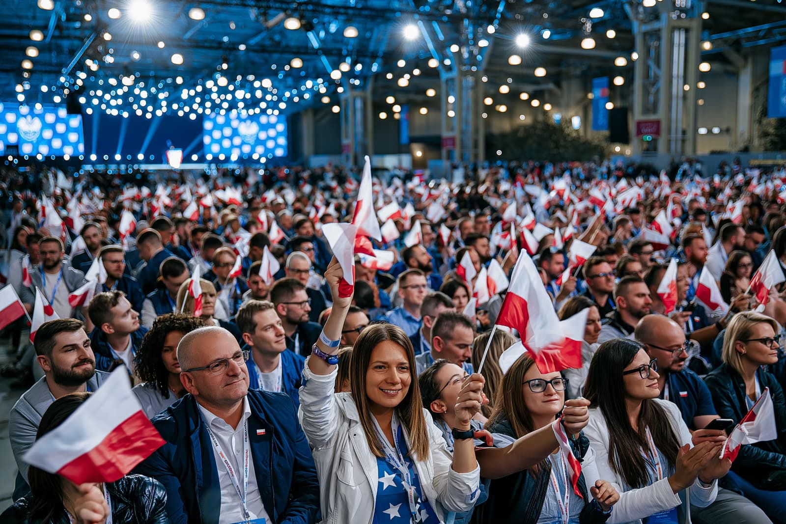 O mulțime arhiplină în sala de expoziții fluturând steaguri mici sub iluminatul puternic al evenimentului de lansare a campaniei AfD Magdeburg, cu o scenă în depărtare.