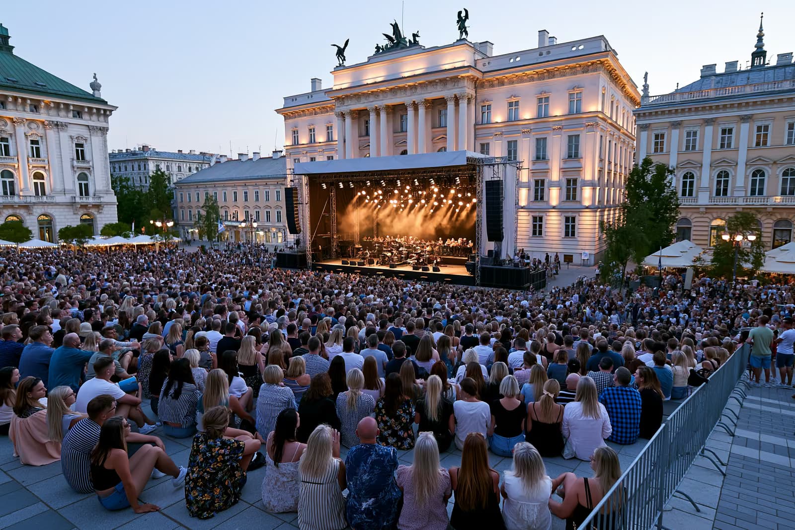 O mulțime se adună la amurg într-o piață istorică din Berlin, unde o scenă de orchestră în aer liber este iluminată pe fundalul unor fațade impunătoare.