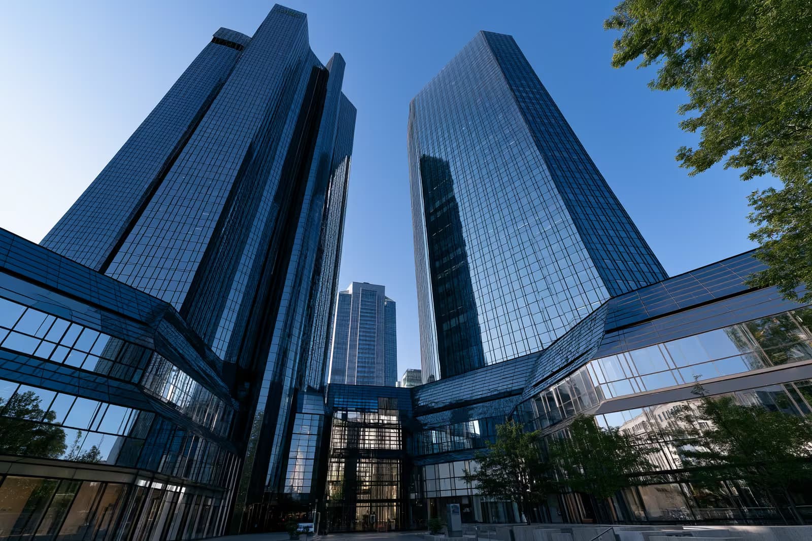 Turnuri bancare gemene din sticlă din Frankfurt strălucind pe un cer albastru strălucitor văzute de jos.
