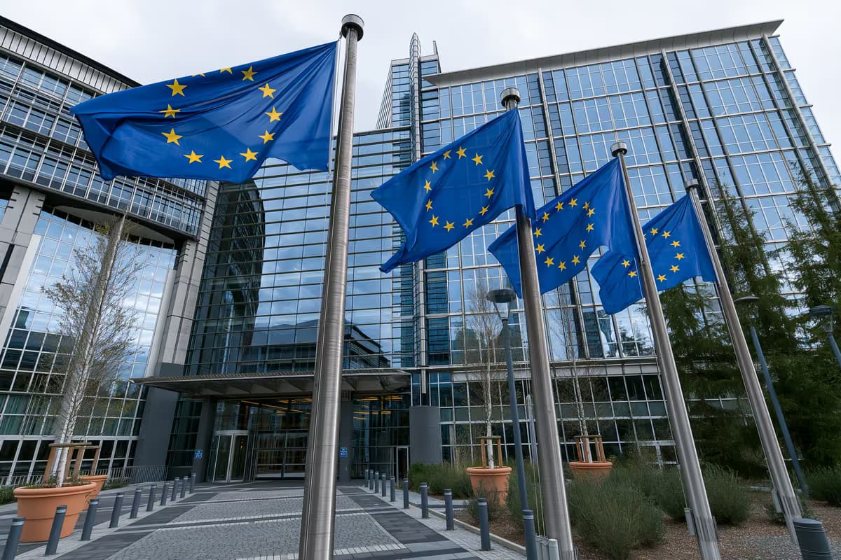 Steaguri ale Uniunii Europene pe catarge în fața unei clădiri moderne de sticlă.