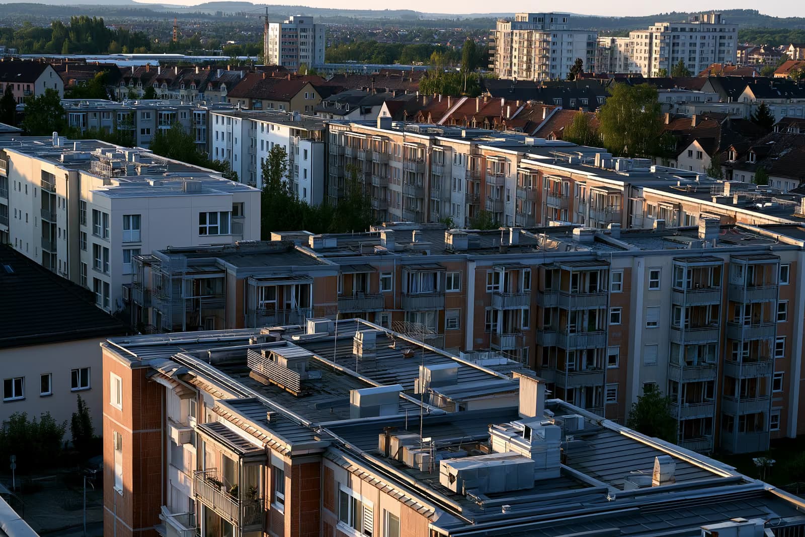 Acoperișuri și guri de aerisire ale clădirilor de apartamente dintr-un oraș german, sub lumina caldă a după-amiezii.
